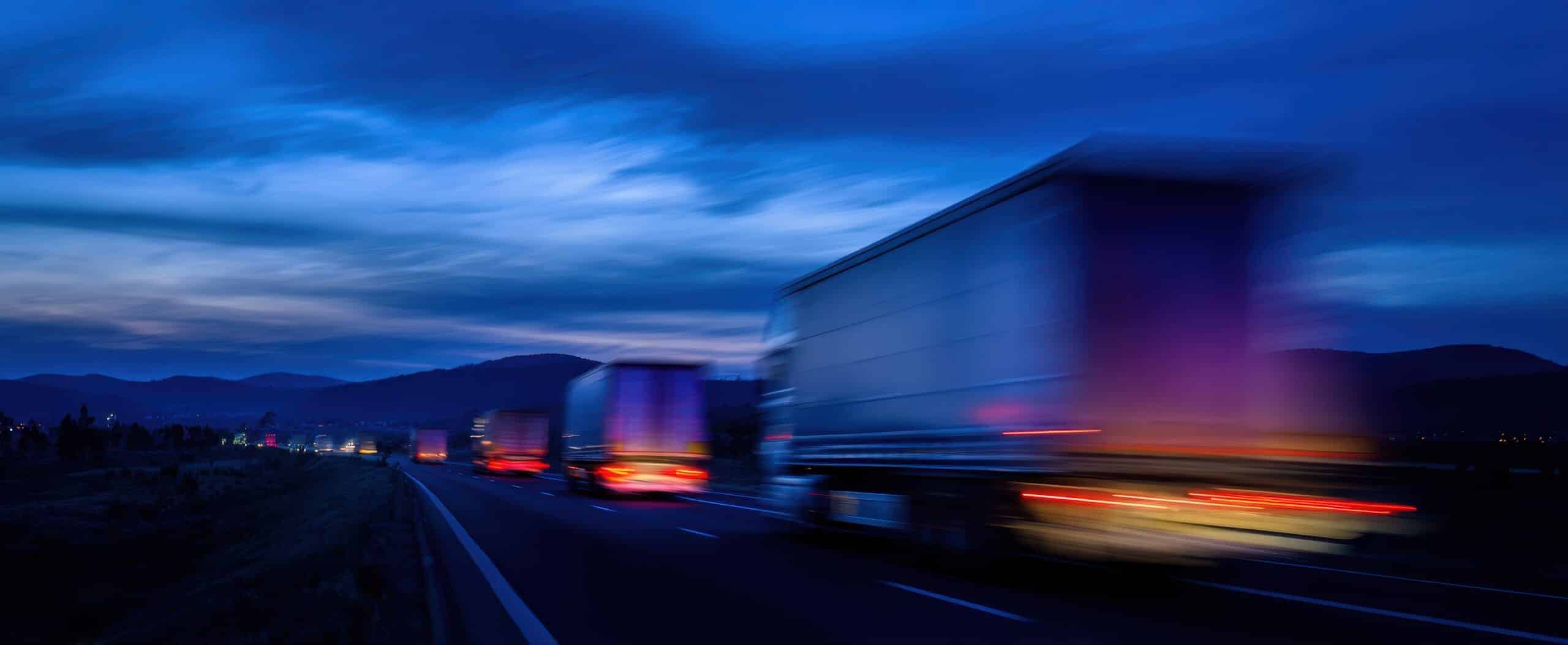 Blurred semi-trucks speeding on a highway at night, illustrating how supply chain issues cause truck accidents due to delivery pressure and unsafe driving conditions.